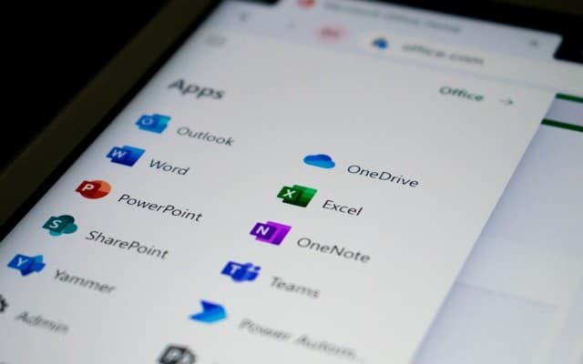 A screen displays the Microsoft Office app menu, showing icons for Outlook, Word, PowerPoint, SharePoint, Yammer, Admin, OneDrive, Excel, OneNote, and Teams. (Photo by Ed Hardie on Unsplash.)